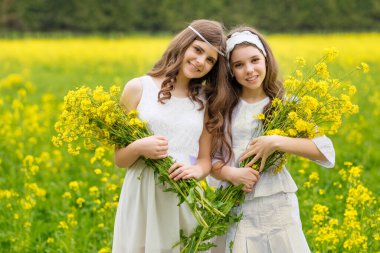 Çiçek açan kolza tohumu tarlasında iki kız yürüyor..