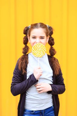 Sarı arka planda büyük bir şekeri olan bir kız..