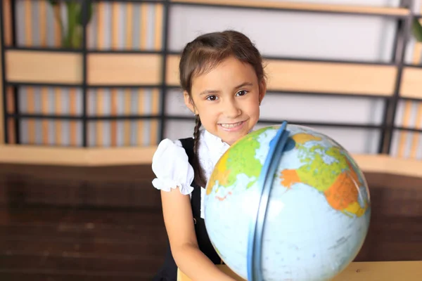 Retrato de uma menina de uniforme escolar com um globo nas mãos. — Fotografia de Stock