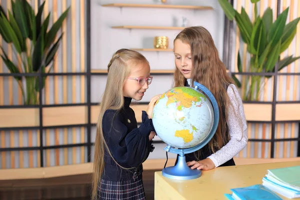 Kinderen in schooluniformen met een wereldbol op kantoor. — Stockfoto