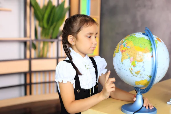 Portret van een meisje in een schooluniform met een wereldbol in haar handen. — Stockfoto