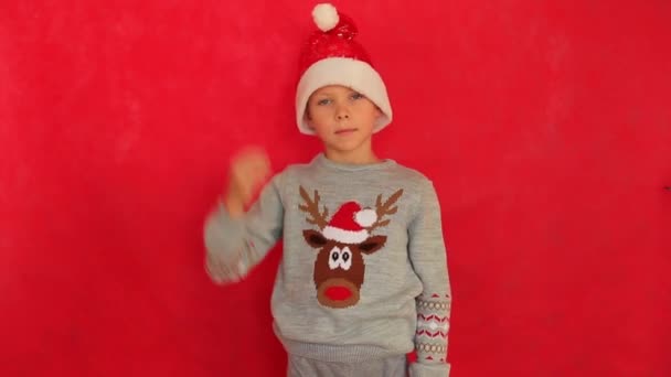 Niño en una gorra de Año Nuevo y suéter sobre un fondo rojo. — Vídeo de stock