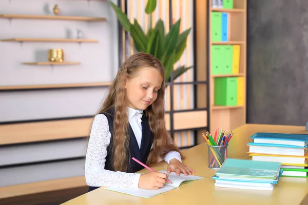Школьница сидит над блокнотами. Девушка пишет в школьной тетради. — стоковое фото