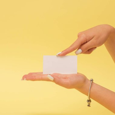Sarı arka planda beyaz kartvizit tutan eller, yumuşak ışıkta yakın planda çekilen fotoğraflar. Markalaşma ve minimalist tasarım için model konsepti.