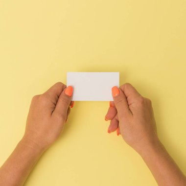 Turuncu manikürlü kadın elleri, boş bir kart gösteriyor. Parlak arkaplanda kafasının üstünden vurulmuş. İş ve reklam için modern minimalist konsept