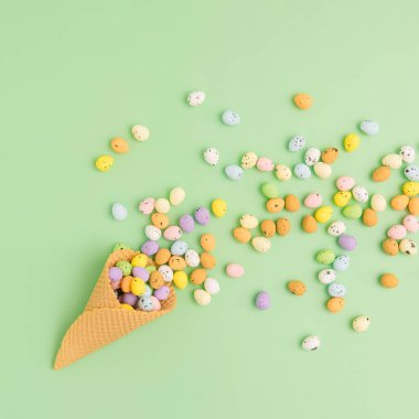 Renkli çikolatalı paskalya yumurtaları nane yeşili arka planda waffle külahından dökülüyor. Yukarıdan fotokopi aletiyle çekilmiş oyuncu düz konum.