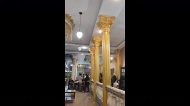 Makassar, Mei 22, 2024 - İnsanların sıcak ve dekoratif bir alanda toplandığı uzun altın klasik sütunlar ve süslü başkentlerle zarif iç mekan.