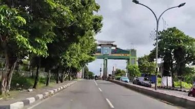 Parepare, 11 Nisan 2024 - Endonezya 'nın Parepare şehrinin çıkış kapısı, yemyeşil ağaçlar ve parlak gökyüzü, araçları ve huzurlu şehir çevresini gösteriyor.