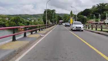 Parepare, 11 Nisan 2024 - Huzurlu bir kentsel bölgede bulutlu bir gökyüzü altında yemyeşil ve tepelerle çevrili sakin bir nehir üzerinden araçlar köprüden geçiyor.