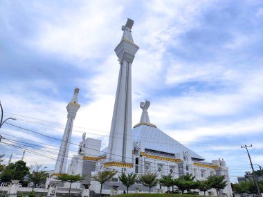 Bulutlu bir gökyüzünün altında uzun minareleri ve modern İslam mimarisi olan büyük bir cami. Şehir ortamında önemli bir dini eser ve ibadet yeri..