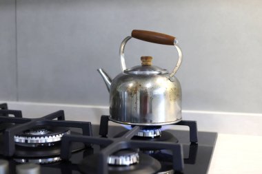 Modern sertleştirilmiş cam bir mutfakta yanan bir gaz sobasının üzerinde metal çaydanlık ısıtma suyu.