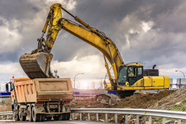 Kazıcı, İspanya 'da bir yamaç inşaatı için bir kamyonu toprakla dolduruyor.