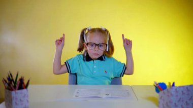 Gözlüklü genç bir öğrenci masasında açık bir egzersiz kitabıyla parlak sarı bir zemine karşı komik hareketler yapıyor. Okul çocuğu yaramazdır, dans eder. Öğrenci kız