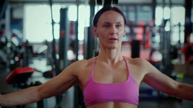 Modern bir spor salonunda halat çekme egzersizi yapan formda bir kadın sırt ve omuz egzersizine odaklanmış. Güç eğitimine yoğun odaklanma: Pembe spor sutyenli kadın kontrollü kablo direnci hareketi uyguluyor. Çalışma ortası yoğunluğu