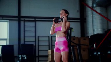 Spor salonunda halterle egzersiz yapan bir kadın. Pembe bluzlu ve şortlu spor kadınlarının aktif fitness eğitimi. Vücut geliştirme egzersizi yapan antrenör..