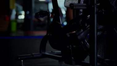 Pembe atletizm giymiş bir kadın loş bir spor salonunda hava bisikleti kullanıyor. Kararlı bir sporcunun durağan bir bisiklette ter içinde kalması. Formda bir kadının sıkı bisiklet sürerken tüm vücudunu çekmesi, fonksiyonel fitness ayarına odaklanmış..