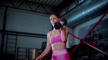 Spor salonunda halterle egzersiz yapan bir kadın. Pembe bluzlu ve şortlu spor kadınlarının aktif fitness eğitimi. Vücut geliştirme egzersizi yapan antrenör..