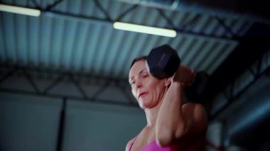 Spor salonunda halterle egzersiz yapan bir kadın. Pembe bluzlu ve şortlu spor kadınlarının aktif fitness eğitimi. Vücut geliştirme egzersizi yapan antrenör..