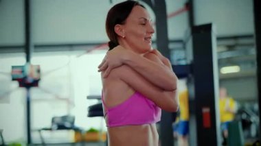 Pembe atletik giysili kadın, yoğun bir antrenmanın ardından oldukça yorgun görünüyor. Kendini işine adamış bir sporcunun loş bir spor salonunda soluklanmasına yakın çekim. Zinde bir kadının yüzünde azim ve kararlılık var. İyileşiyor.