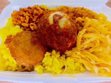 Nasi kuning, or yellow rice, is a traditional Indonesian dish made from rice cooked with turmeric. Served with boiled egg, potato cakes, tempeh, and shredded egg.