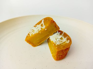 Kue Lumpur ya da Çamurlu kek rendelenmiş hindistan cevizi parçacıkları, ikiye bölünmüş, yuvarlak bir tabakta servis ediliyor, beyaz arka planda izole edilmiş..