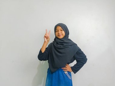 Siyah tesettürlü bir kız, iki parmağı yukarıda, beyaz arka planda soyutlanmış..