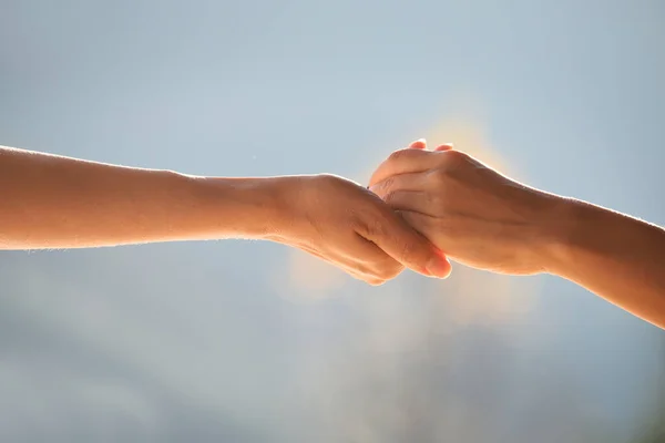 Two hands supporting each other, holding each other against the gentle blue natural background.