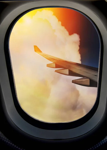 Airplane porthole with a wheel on the plane wing and clouds in the blue sky.