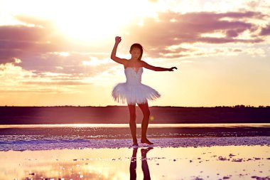 Genç bir balerin gölün üzerinde batan güneşin ışınlarında dans ediyor..