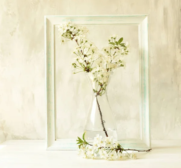 Branches with white cherry flowers in a transparent glass vase on a gray background and vintage frame. Vintage still life, Easter card.