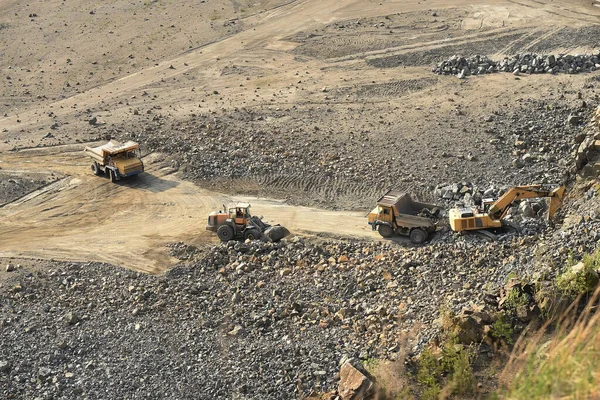 heavy industrial machinery works in a rock loading quarry. A crane loads granite stones in a quarry onto a truck. View from above.