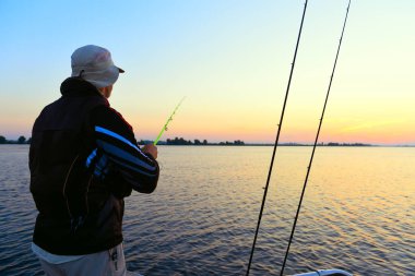 Elinde olta olan erkek bir balıkçı şafak vakti bir tekneden balık yakalar..