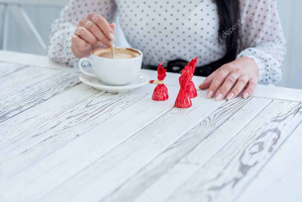 A cup of coffee with milk and bright confectionery on a white table. the girl's hands stirring with a spoon of coffee and candy. The idea of a diet and proper nutrition.