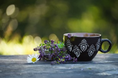 Bahçedeki kaba ahşap bir masada yanında bitki çayı ve kekik olan bir fincan..
