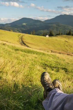 Yeşil çayırlar ve dağ zirvelerinin arka planında kirli yürüyüş botları. Seyahat atmosferi.