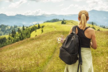 Sırt çantalı bir kız turist dağ manzarası ve çiçek açan çayırlarda.