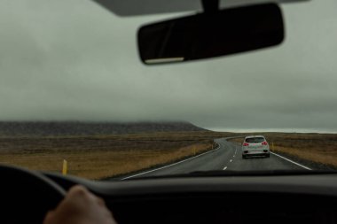İzlanda 'da dolambaçlı bir yoldan geçen bir aracın ön camından dramatik ve bulutlu manzaraya bakın. Dengesiz hava ve seyahat ve keşif hissi..