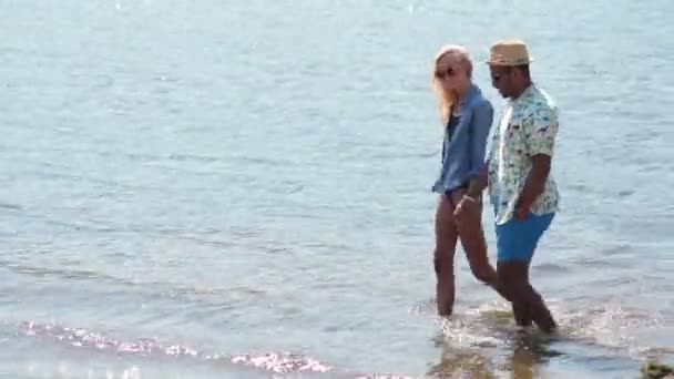 Pareja cogida de la mano caminando en el agua en la playa — Vídeos de Stock