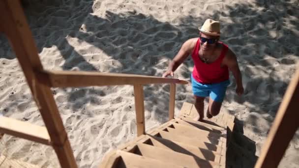 Чоловік піднімається драбиною на дерев'яному будинку на пляжі — стокове відео