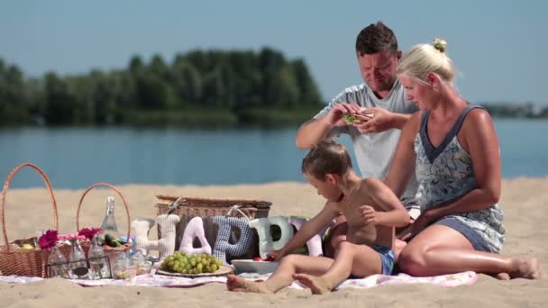 Gezin met kind genieten van picknick op de rivier bank — Stockvideo