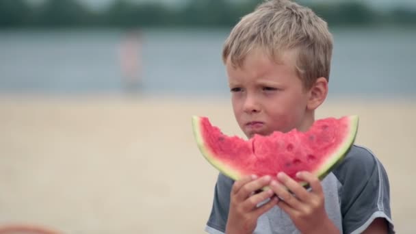 Chłopiec litttle jedzenie pyszne arbuzy na plaży — Wideo stockowe