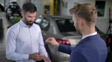 Otomobil galerisinde araba anahtarı alan mutlu bir erkek alıcı.