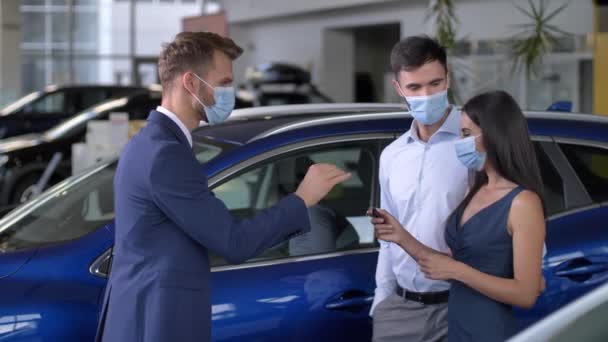 Feliz pareja en máscaras tomando la llave del coche en la sala de exposición — Vídeos de Stock