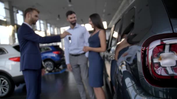Размытая счастливая пара получает ключи от машины в автосалоне — стоковое видео