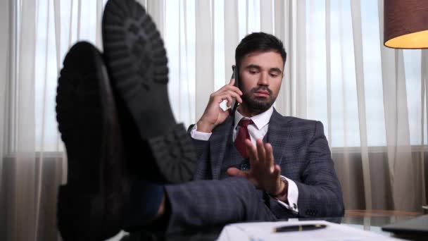 Magabiztos férfi beszél telefonon lábakkal az asztalon — Stock videók
