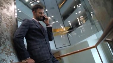 Asansör kabininde neşeli bir işadamı konuşuyor.
