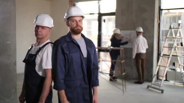 Dwóch budowniczych w kaskach pozujących w miejscu pracy — Wideo stockowe
