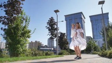 Şehir parkında dans eden küçük kızla neşeli bir anne.