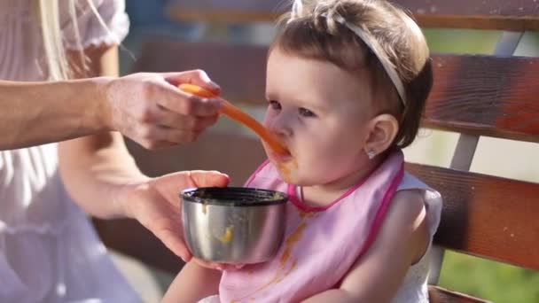 Догляд за матерями руки годують дівчинку на лавці — стокове відео