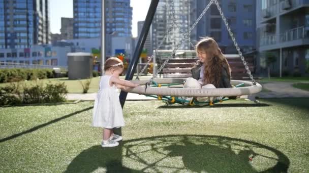 Un an bébé balançant sœur aînée en plein air — Video